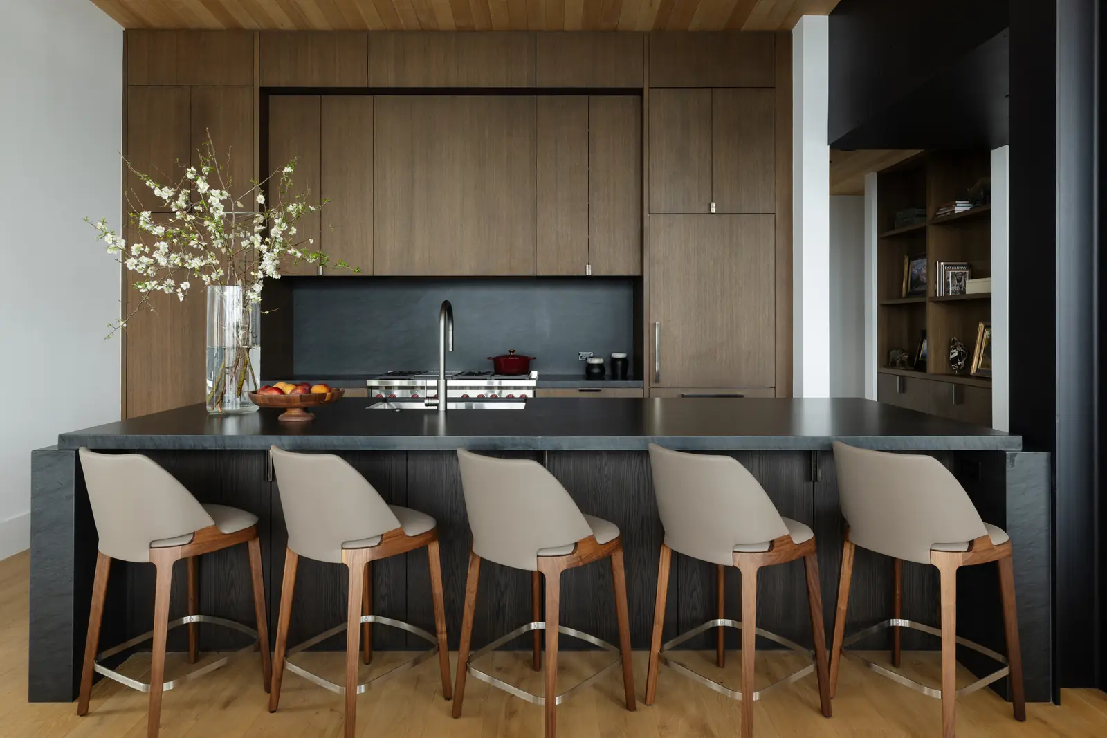 Kitchen with a dark stone island, walnut cabinetry and leather stools