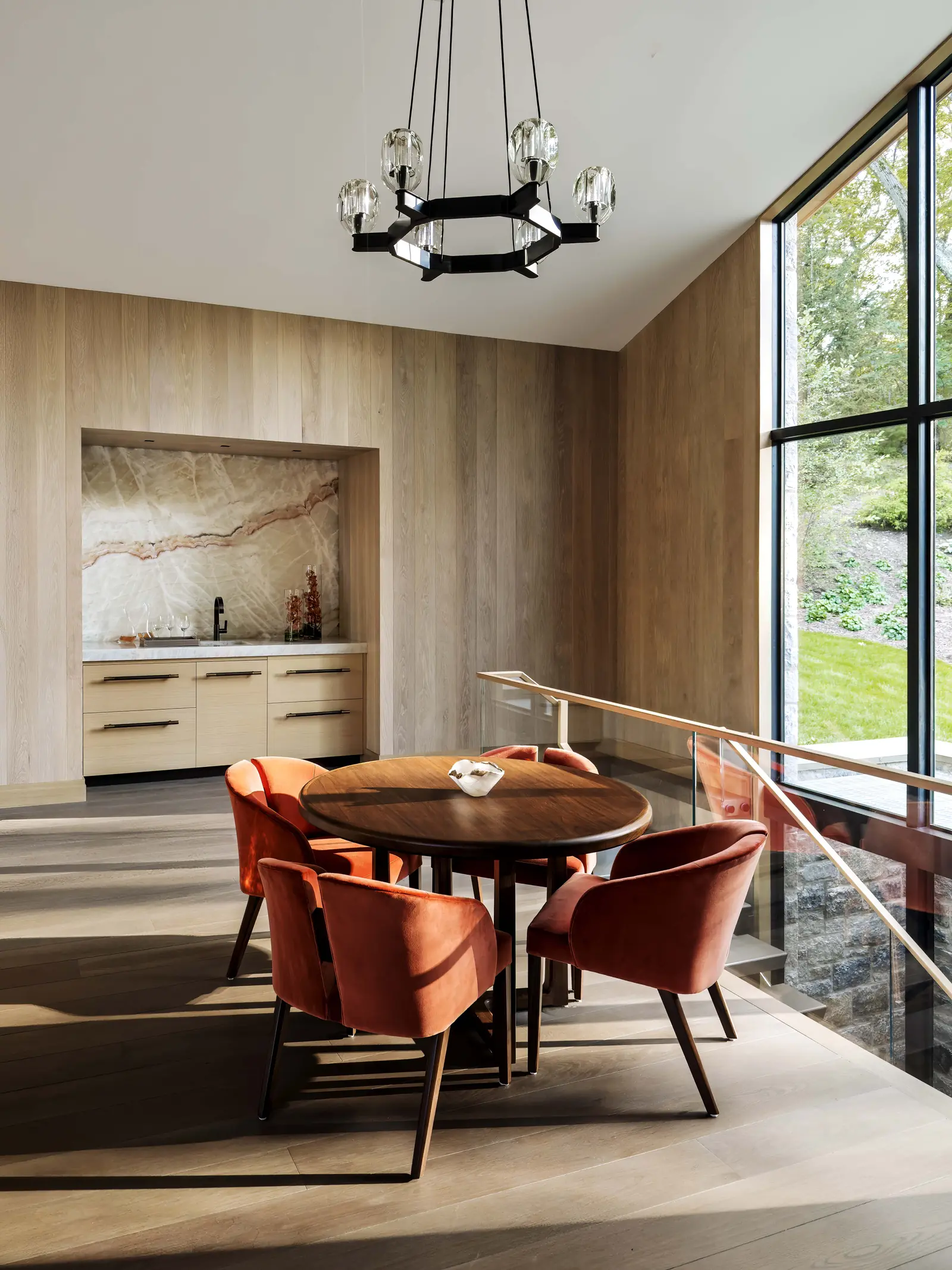 Breakfast table with rust velvet chairs beside a wall of glass